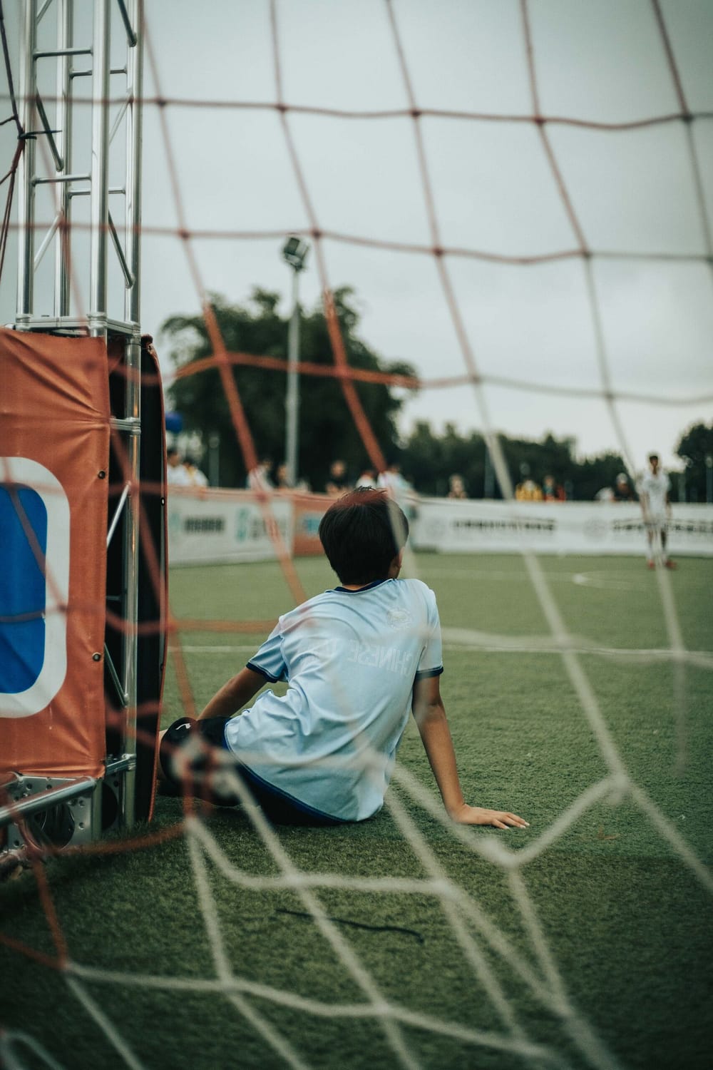 young person sitting on grass in front of soccer goal
