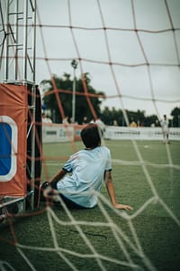 young person sitting on grass in front of soccer goal